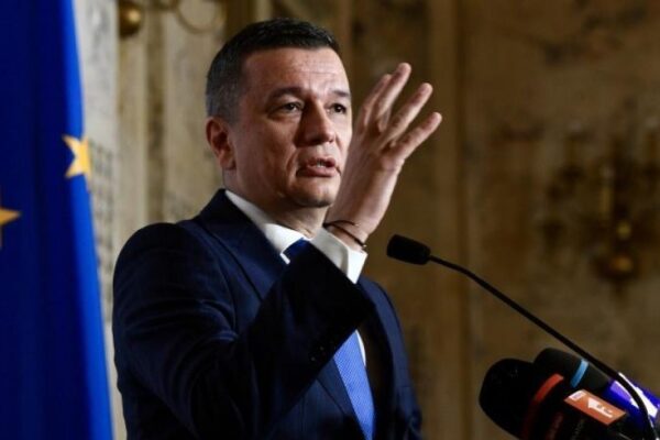 Bărbat ținând discurs la pupitru, steagul UE